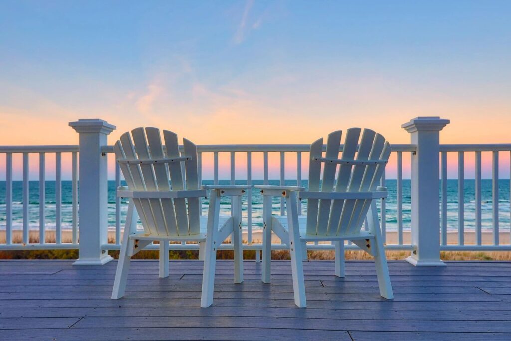 Two white chairs on a deck overlooking the ocean.