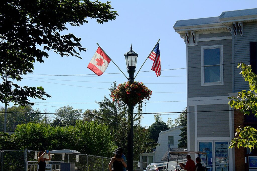 The flags of America and Canada on one pole with trees around