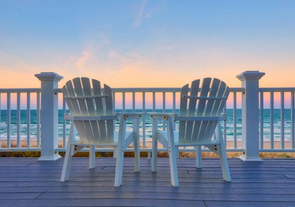 Two white chairs on a deck overlooking the ocean.