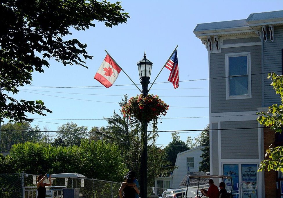 The flags of America and Canada on one pole with trees around